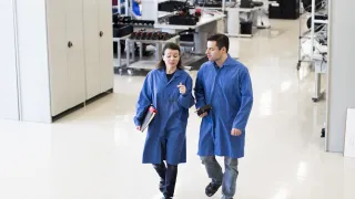 Sinitakkiset mies ja nainen keskustelevat tehtaan laboratoriossa