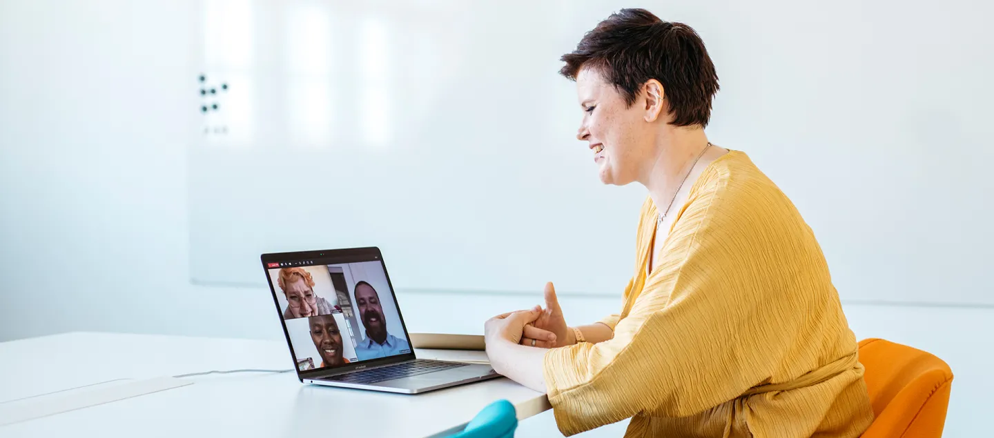 A laughing woman is participating in a remote meeting using a laptop.