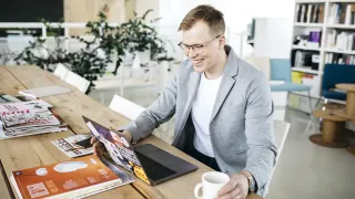 Henkilö istuu kannettavan tietokoneen edessä ja hymyilee.
