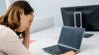 Stressaantunut naine nojaa päällään käteensä istuessaan tietokoneen ääressä.
