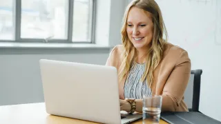 Hymyilevä nainen tekee työtä kannettavalla tietokoneella.