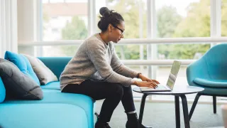 Nainen istuu sohvalla ja kirjoittaa tietokoneella