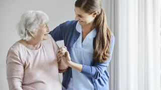 Vanhustyön ammattilainen auttaa ikäihmistä hymy huulilla.