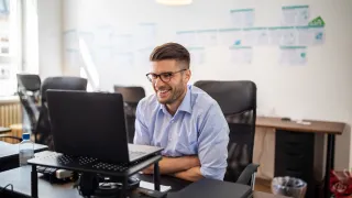 Mies hymyilee kannettavan tietokoneen ääressä