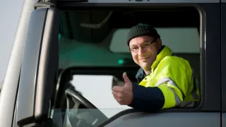 Ajoneuvoyhdistelmän kuljettaja katsoo hymyillen ulos ajoneuvon ikkunasta. 