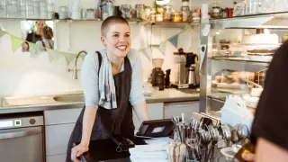 Työntekijä hymyilee leveästi kahvilaympäristössä.