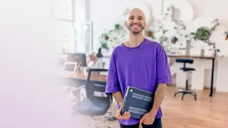 työntekijä katsoo kameraan ja hymyilee tiomistossa kannettava tietokone käsissään