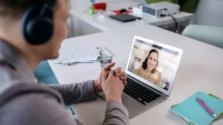 Henkilö on videopuhelussa toisen kanssa kannettavalta tietokoneelta.