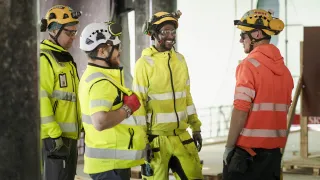 Joukko rakennusmiehiä keskustelee rakennustyömaalla.