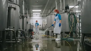 Tehdastyöntekijä pesee tehtaan lattiaa letkulla