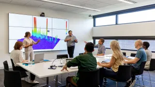 Ryhmä työntekijöitä kokoushuoneessa katsoo ruutua