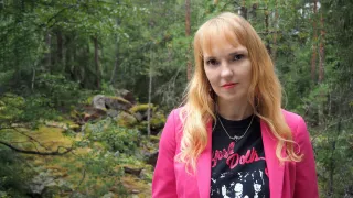 Vaaleahiuksinen nainen vaaleanpunainen bleiseri päällä katsoo kameraa ja taustalla näkyy metsää