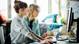 Kaksi naiskollegaa keskustelee tietokoneen äärellä