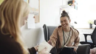 Terapeutti keskustelee asiakkaan kanssa hymyillen ja ojentaa nenäliinapaketin