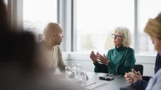 Ihmiset juttelevat kokouksessa. Etualalla näkyy ihmisen varjo.