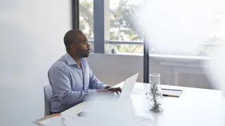 Bisnesmies tekee töitä kannettavalla tietokoneella ja katsoo ulos ikkunasta