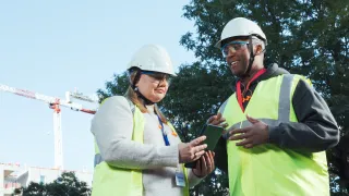Kaksi henkilöä keskustelee ulkona työmaalla ja katsoo tablettia.
