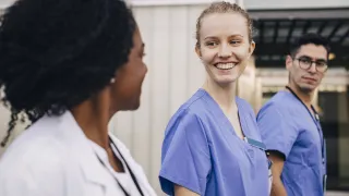 Kolme hoitajaa kävelee ja hymyilee toisilleen