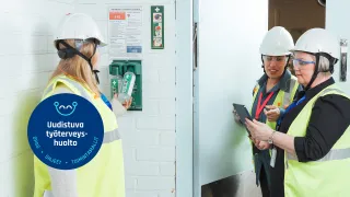 Kolme henkilöä henkilönsuojaimiin pukeutuneena tarkastamassa mm. silmähuuhdetta.