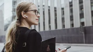 Nainen katsoo kaukaisuuteen puhelin kädessä ja kuuloke korvassa