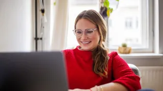 Nainen katsoo tyytyväisenä hymyillen webinaaria.