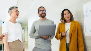 Kolme työkaveria keskustelee valoisassa toimistossa.