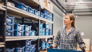 Nainen kantaa laatikoita varastossa.