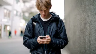Nuori poika kulkee kadulla ja katsoo puhelintaan kädessä