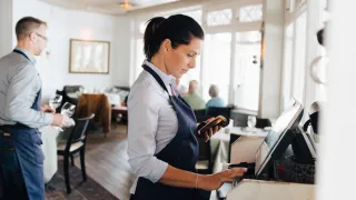 Tarjoilija työskentelee tietokoneen ääressä ravintolassa.