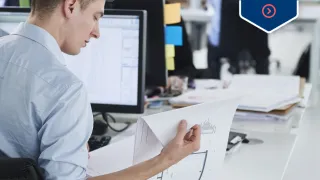 Mies selaa paperinippua työpöydän ääressä toimistossa