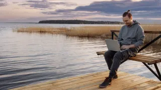 Miesoletettu istuu hymyillen laiturilla kannettava tietokone sylissään. 