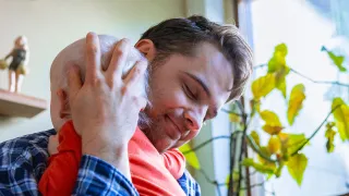 Isäoletettu halaa pientä lasta ja hymyilee