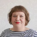 Lyhythiuksinen nainen mustavalkoinen raitapaita päällä hymyilee kameralle