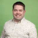 Mies katsoo kameraan ja on valokuvattavana vihreää taustaa vasten