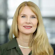 Vaaleahiuksinen nainen vihreä paita päällä katsoo kameraan.