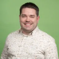 Mies katsoo kameraan ja on valokuvattavana vihreää taustaa vasten