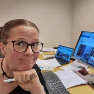 Henkilö katsoo kameraan ja on kuvattavana toimiston työpisteellä.